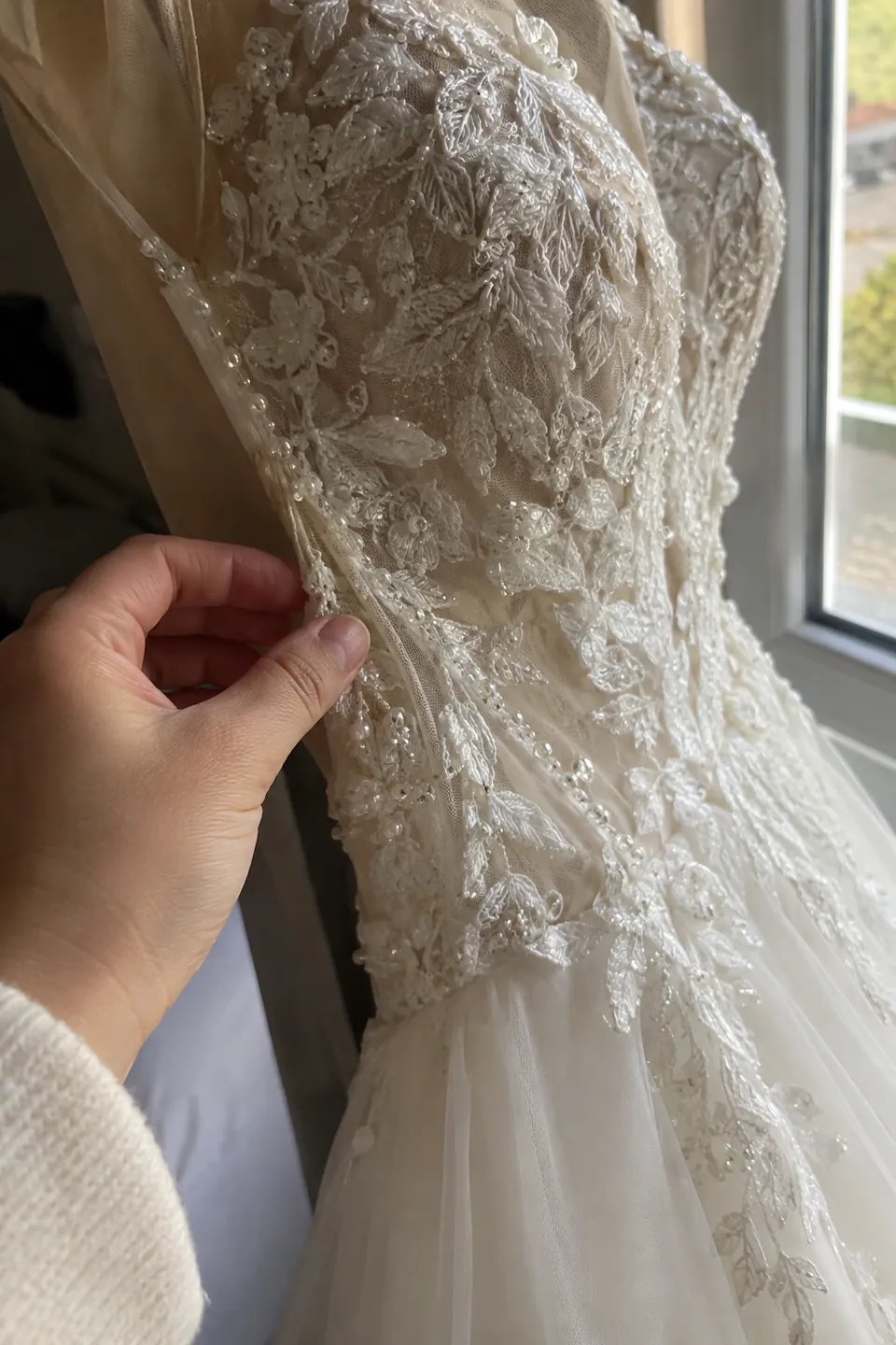 Close-up of a secondhand gown bodice held by a window, with a hand checking the beaded seams