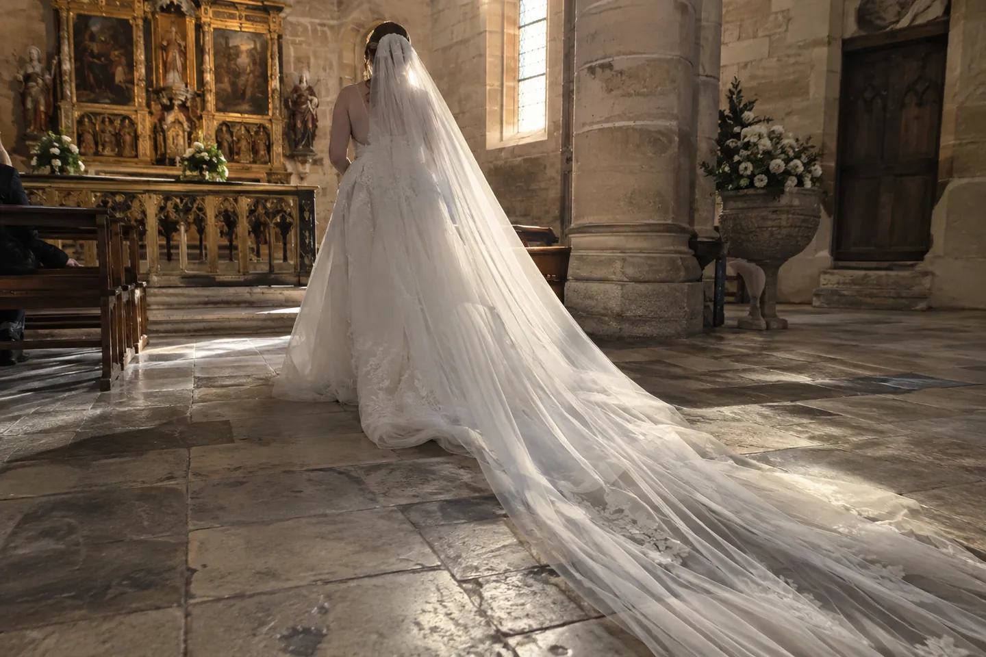 A bride from behind with a long cathedral-length tulle veil on a stone church floor